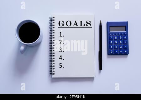 Goals text on notepad with pen, calculator and a cup of coffee on white background Stock Photo