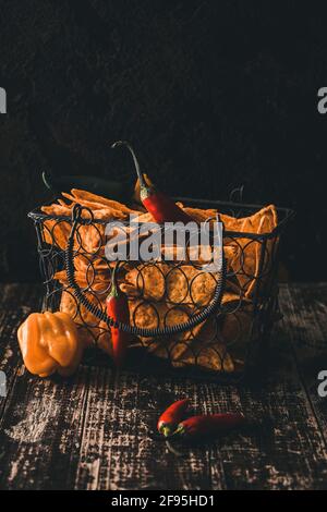 Spicy nachos corn chips and chilis placed in a basket on a wooden table with dark background. Stock Photo