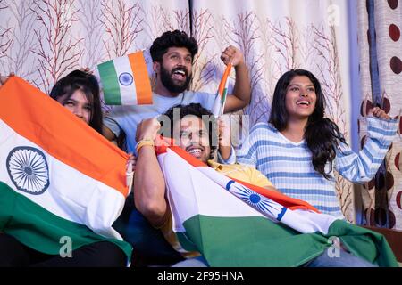 Group of friends shouting India India while watching sports match on television at home - Concept of group of people supporting Indian cricket people Stock Photo