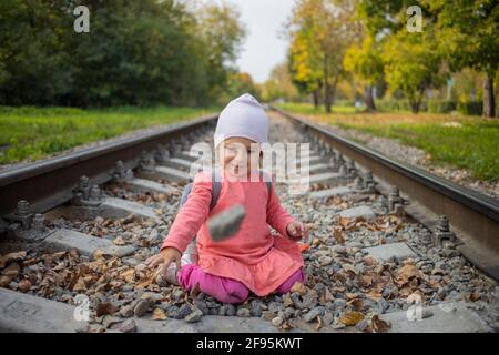 little girl sitting on the railroad tracks. toddler plays on railroad in forest Stock Photo