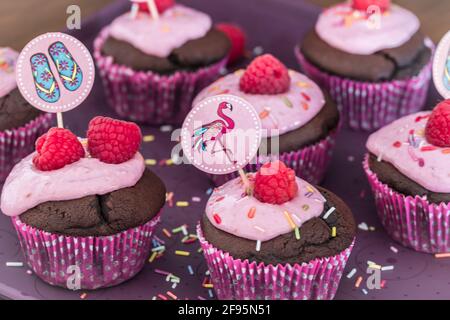 Chocolate cupcakes with raspberry cream, whole raspberry, sugar sprinkles and summer decoration. Closeup. Stock Photo