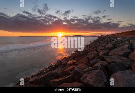 Sunset at Aberavon beach on an incoming tide with Swansea on the horizon, South Wales, UK Stock Photo