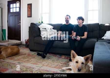 Father and son playing video games together on the couch. Stock Photo
