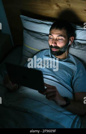 Man lying on bed with tablet in darkness Stock Photo