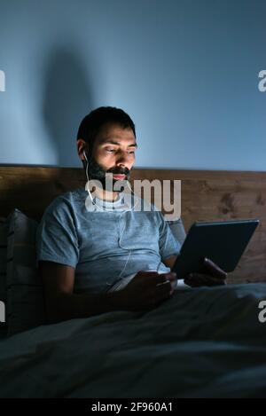 Young man in headphones using tablet on bed at night Stock Photo