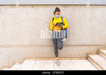 Active woman with sportswear tablet and mask waiting on stairs Stock Photo
