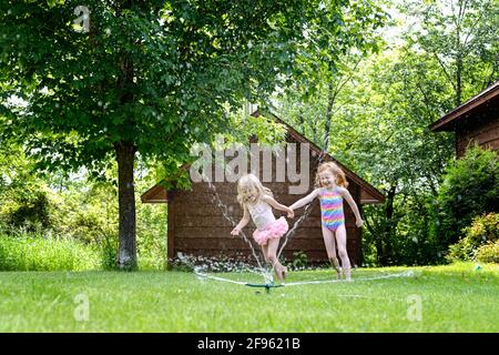 Two cute little girls playing outdoors in a water sprinkler. Stock Photo