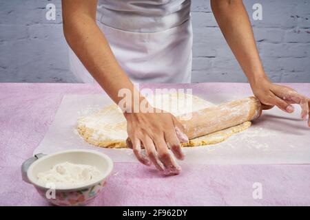 Flattening the dough with the rolling pin to prepare the alfajores. Stock Photo