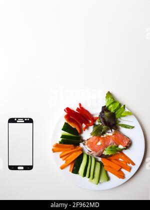 smartphone frame & white plate with vegetables & salmon on white table Stock Photo