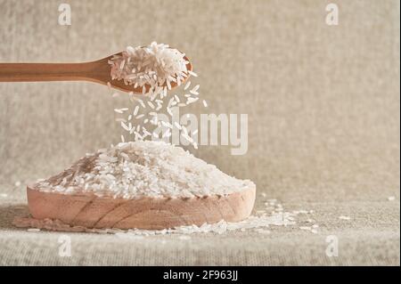 Close up of a wooden spoon pouring raw white rice on a wooden plate Stock Photo