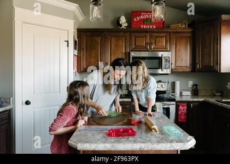 Mother making gingerbread houses with kids daughters at home Stock Photo