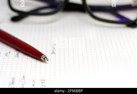 Red ballpoint pen on the white pages of an open notebook with a pair of eyeglasses in the background. Inspiration and storytelling. Stock Photo