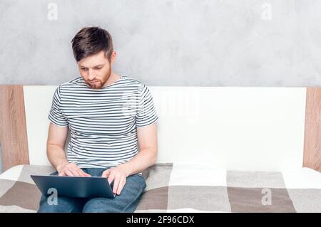 Young man working on a laptop in bed at home. Concept Working remotely Stock Photo