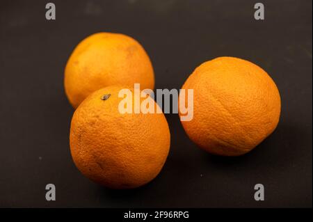 Three fresh juicy oranges on a black background. Close-up selective focus. Stock Photo