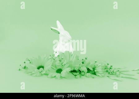 Happy Easter concept. Beautiful white porcelain rabbit with flowers on pastel green color background. Greeting card. Creative design. Copy space. Stock Photo