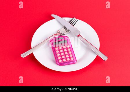 Pink calculator, knife and fork on a white plate with red background Stock Photo