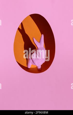 Minimalist Easter concept. Creative layout made with pink porcelain rabbit inside the orange egg on bright pink background. Copy space. Stock Photo
