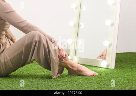 woman looking at her reflection in illuminated mirror for dressing room sitting on floor in studio Stock Photo
