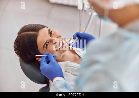 Portrait of young dentist in gloves examining teeth of female client in the hospital Stock Photo