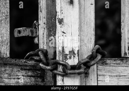 A white wooden gate, locked with an old rusty iron chain. Stock Photo