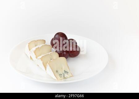 pieces of camembert or brie cheese with red grapes on plate isolated on white background, soft cheese covered with edible white mold view from above, Stock Photo