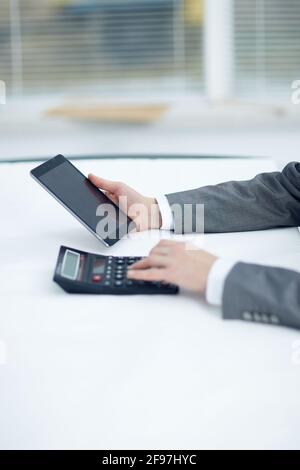 Manager holds a tablet in his left hand in his right hand works on a calculator Stock Photo