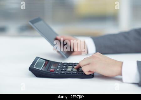 Manager holds a tablet in his left hand in his right hand works on a calculator Stock Photo