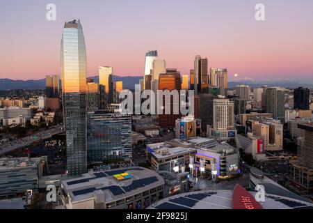 Dusk with moon rising over the mountains behind downtown Los Angeles skyline aerial Stock Photo