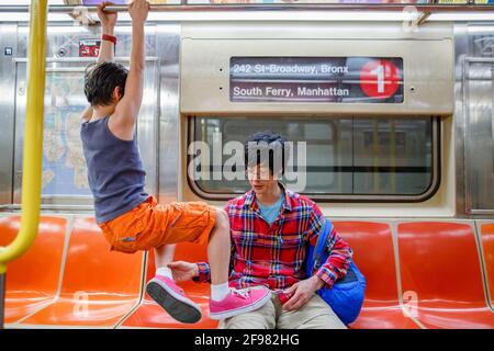Small boy hangs from handrail in NYC subway and father pulls him down Stock Photo