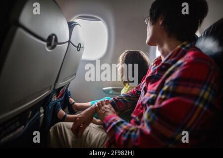 A little girl and father sit together on airplane looking out window Stock Photo