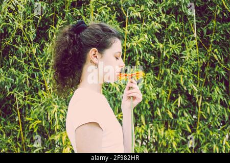 woman smelling orange flower with green bamboo leaves Stock Photo