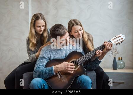 Dad plays the guitar for daughters. At home with your family Stock Photo
