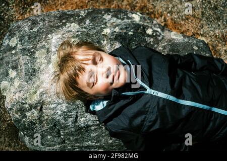 Child lying down on rock and enjoying the first warm sun rays on face