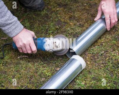 hands of man cutting the stove pipe, working with portable grinder machine on the grass Stock Photo