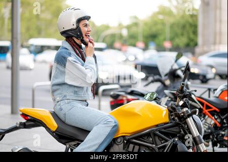 Right side shot of a young woman riding a motorcycle fastening her protective helmet Stock Photo