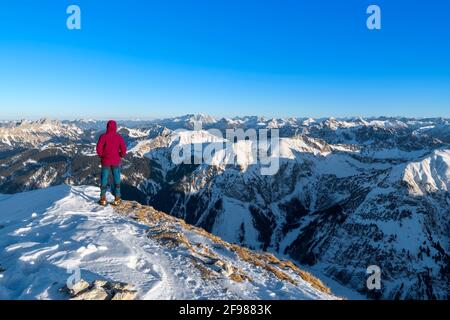 In winter, mountaineer stands on a summit above the Tannheim Valley and looks into the distance. Allgäu Alps, Tyrol, Austria Stock Photo