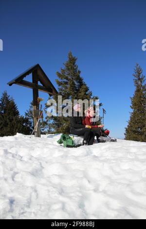 Winter hike 2 women to the Grünkopf near Mittenwald, Europe, Germany, Bavaria, Upper Bavaria, Isar Valley, Kreuz, snack Stock Photo