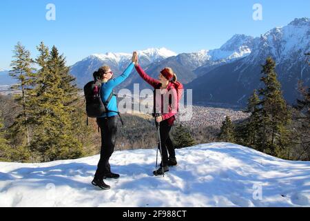 Winter hike 2 women to the Grünkopf near Mittenwald, Europe, Germany, Bavaria, Upper Bavaria, Isar Valley, clapping on a mountain peak Stock Photo