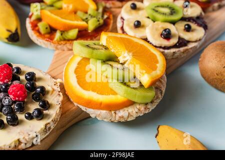Crispy puffed rice cakes on table with fresh fruit kiwi banana apple blueberries and orange on the table - close up view on healthy organic vegetarian Stock Photo