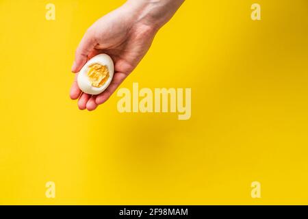 Close up on hand holding boiled egg with yolk in front of yellow background Stock Photo