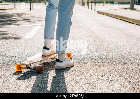close-up take of the legs of an unrecognizable man on a skateboard on the street asphalt. He is projecting a hard shadow on the asphalt. Stock Photo