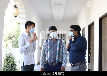 Front view of three Indian men with face masks having a conversation standing outside the clinic Stock Photo
