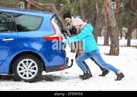 Couple pushing broken car on winter day Stock Photo