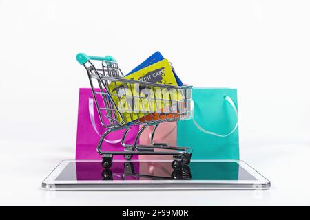 tablet, mini shopping cart with credit cards and colourful paper bags isolated on white Stock Photo