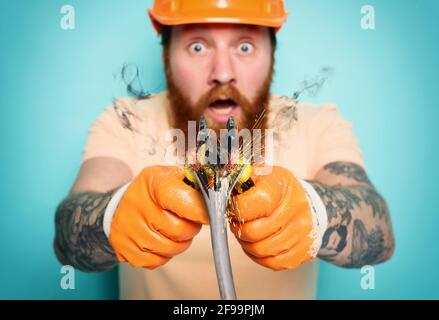 Incompetent worker electrician is unsure about his work. cyan background Stock Photo