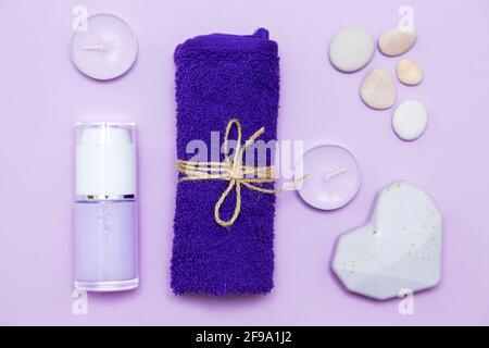 Scented candles, towel, lotion and pebbles on a lilac background. Top view, copy space, flat lay. Spa and body care concept. Stock Photo