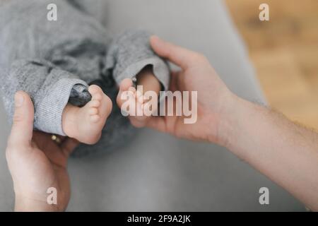 Photo of young mother or doctor hands holding little feet barefoot of newborn on gray background. Happy moment of parenthood. Close-up. Stock Photo