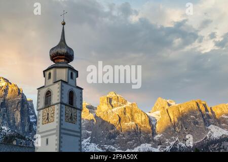 Colfosco, Alta Badia, Dolomites, South Tyrol, Italy. The bell tower of the San Vigilio church with the Sella group in background Stock Photo