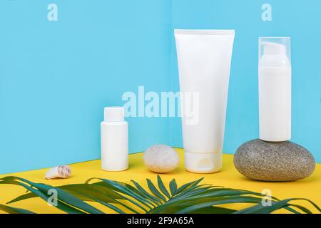White blank cosmetic tube, bottle with sunscreen, sun cream, moisturizing lotion, rock and green leaf on blue, yellow background. Concept skin care in Stock Photo