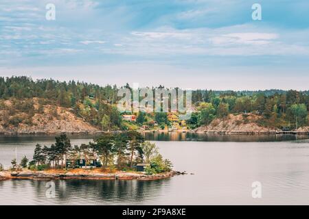 Sweden. Many Beautiful Swedish Wooden Log Cabins Houses On Rocky Island Coast In Summer Day. Lake Or River Landscape Stock Photo